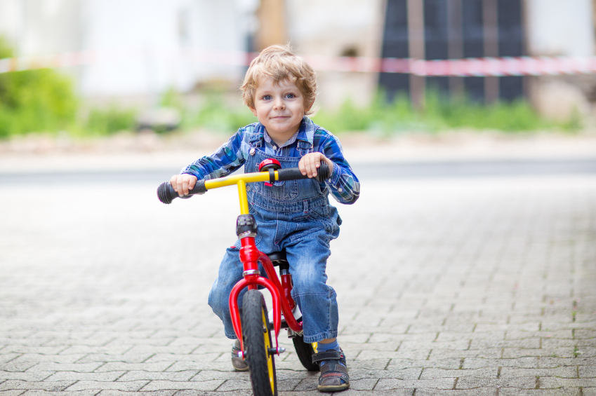Little toddler boy learning to ride on his first bike